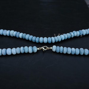 Op de afbeelding: Een lichtblauwe edelsteenketting met een zilveren sluiting. De ketting is gemaakt van ronde kralen en is ongeveer 45 centimeter lang.