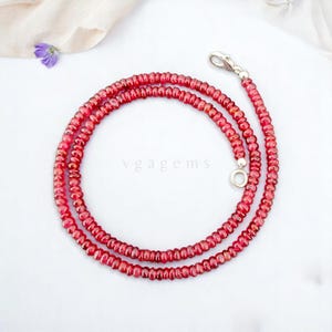 May include: A red ruby gemstone necklace with a silver clasp. The necklace is made of small, round beads and is approximately 18 inches long.