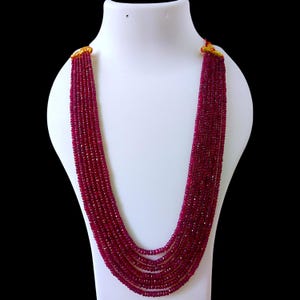 Op de afbeelding: Een lange, meerstrengs ketting gemaakt van dieprode robijn kralen. De ketting wordt getoond op een witte mannequinbuste.