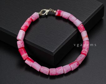 May include: A pink and red beaded bracelet with a silver clasp. The bracelet is made of rectangular beads in varying shades of pink and red. The text "vgagems" is visible on the right side of the image.