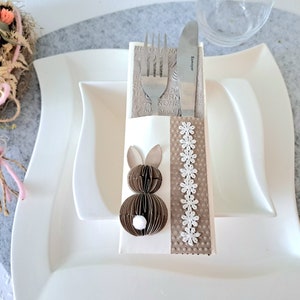 Könnte beinhalten: Ein weißer Serviettenhalter mit einem braunen Hasendesign und weißer Spitzenborte. Eine Gabel und ein Messer sind in den Halter gelegt.