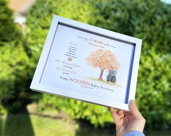 May include: A framed print celebrating a 5th wedding anniversary. The white framed artwork features a tree with two figures under it, with text that reads "Happy Wooden Wedding Anniversary" and the date "21st May 2020".