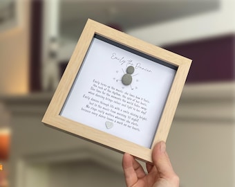 May include: A square light wood frame containing a white background with the text Emily the Dancer, a poem, and a figure made of two gray pebbles with drawn limbs. Small gray hearts surround the figure, and a single gray heart sits below the text.