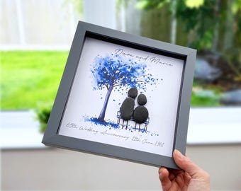 May include: A square framed wall art piece featuring a watercolor illustration of a blue tree and a bench. Two figures made of smooth dark gray pebbles sit on the bench. The text reads Dave and Marie, 65th Wedding Anniversary 11th June 1961.