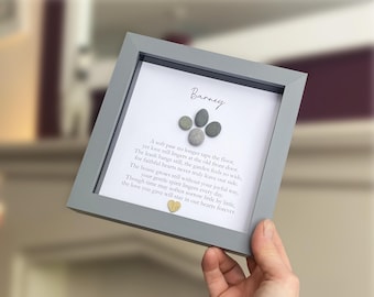 May include: A square gray frame containing a white background with the name Barney, a paw print made of four gray pebbles, a poem about pet loss, and a small gold heart at the bottom. The text reads: A soft paw no longer taps the floor.