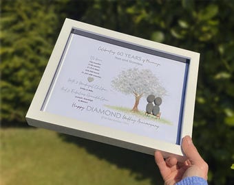 May include: A framed print celebrating a 60th wedding anniversary. The artwork features a tree with pebble art figures, text that reads "Happy Diamond Wedding Anniversary," and the date December 21, 1963. The frame is white.