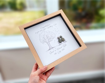 May include: A square light wood frame containing a white print of a tree with heart-shaped leaves and two figures sitting on a bench made of grey pebbles. The text reads: Congratulations as you renew your Wedding Vows, Sarah & Michael Taylor, 11th July 2026.
