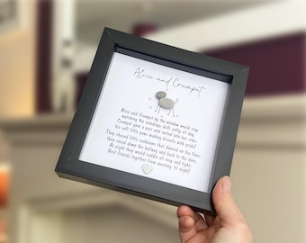 May include: A black square frame containing a white background with the text Alice and Crumpet, a poem about a cat and dog, and a small pebble art figure of an animal with a heart shape at the bottom, all displayed under a clear glass cover.