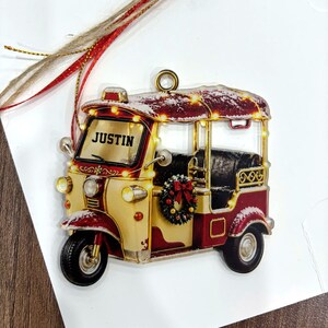 A decorative ornament featuring a vintage-style red and gold vehicle with the name "JUSTIN" displayed on the front.