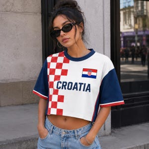 A woman wearing a white and red Croatia jersey stands in front of a building, with the Croatia flag visible on her shirt.