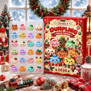 May include: A Charlie's Dumpling Advent Calendar 2026 box featuring a festive Christmas tree and holiday decorations, alongside a clear plastic tray containing twenty-four colorful, small, smiling dumpling-shaped ornaments with various holiday accessories.