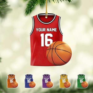 May include: A red basketball jersey ornament with the text "YOUR NAME" and the number "16" in white. A basketball is next to the jersey. Below are smaller ornaments in orange, blue, purple, yellow, and green, each with a jersey and basketball.