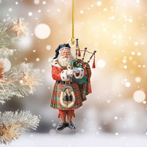 May include: A Christmas ornament depicting Santa Claus in a red coat and plaid kilt, playing bagpipes. The ornament has a gold string for hanging and the text "Your name" on the hat. The background is a blurred winter scene.
