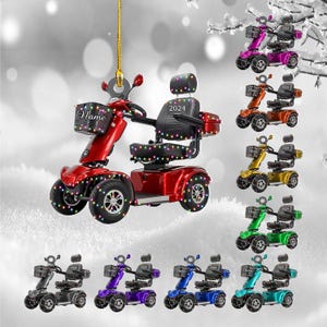 May include: A red mobility scooter ornament with the word "Name" on the basket and "2024" on the seat. Additional scooters in various colors are also shown, including purple, orange, yellow, green, black, blue, and teal.