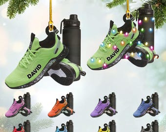Könnte beinhalten: Eine Sammlung von Laufschuh-Ornamenten in verschiedenen Farben, jeweils mit dem Namen "DAVID" bedruckt. Jedes Ornament wird mit einer schwarzen Wasserflasche kombiniert. Einige sind mit Lichterketten verziert, ideal für die Weihnachtsdekoration.