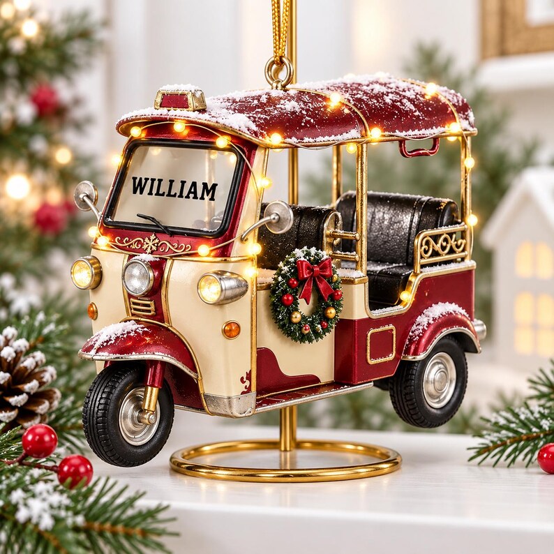 A decorative ornament in the shape of a red and white vehicle, with the name "William" displayed on the front. The ornament is illuminated with lights and is placed on a stand, surrounded by pine branches and other holiday decorations.
