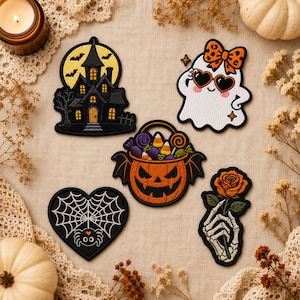 May include: Five embroidered Halloween patches featuring a haunted house with a yellow moon, a white ghost wearing heart-shaped sunglasses and a bow, a jack-o'-lantern bucket filled with candy, a spider on a web, and a skeleton hand holding a rose.