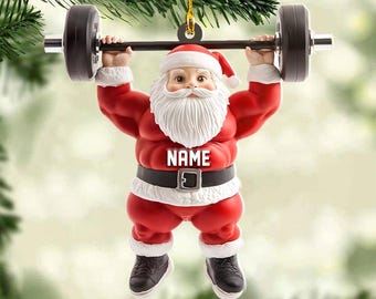 May include: A Christmas ornament of Santa Claus lifting a barbell. Santa is wearing a red suit, black belt, and black shoes. The ornament has the word "NAME" on the belt. The barbell has black weights and silver handles.