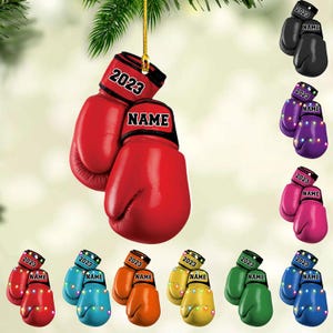May include: Boxing glove ornaments in various colors, each with "2023" and "NAME" printed on the cuff. The ornaments are hanging, with some featuring string lights. Colors include red, black, purple, pink, blue, orange, yellow, green, and blue.