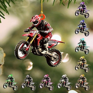 May include: A red and black motocross rider ornament with the word "NAME" on the side. The rider is wearing a red helmet and riding a red and yellow dirt bike. Additional ornaments of riders on motorcycles in various colors are also visible.
