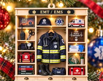 May include: A wooden display ornament featuring an EMT theme with shelves holding miniature items including a jacket, boots, a trauma bag, a first aid kit, a radio, a stethoscope, a toy ambulance, and signs reading EMT / EMS and SAME PEOPLE DIFFERENT DAY.