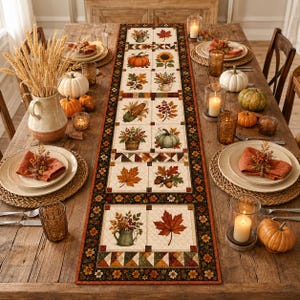 May include: A rectangular fabric table runner featuring a patchwork design with autumn-themed illustrations including pumpkins, sunflowers, acorns, and maple leaves, bordered by a dark floral pattern on a wooden dining table with place settings.