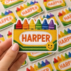 May include: Embroidered patch featuring a crayon box design with the name "HARPER" in orange letters. The box contains colorful crayons in red, orange, yellow, green, blue, and purple. A smiling face is on the lower right.
