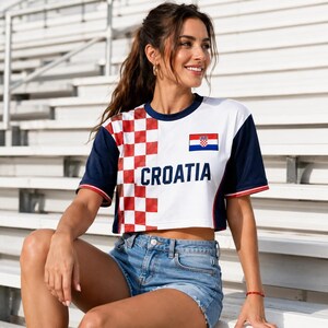 A woman wearing a white and red Croatia jersey is sitting on bleachers, smiling and looking to her left.