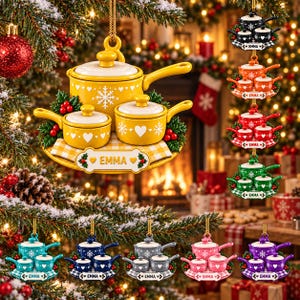 May include: A hanging Christmas ornament featuring a set of three miniature yellow pots on a checkered base, decorated with white snowflakes, hearts, and holly berries. A white plaque at the bottom displays the name EMMA in gold lettering.
