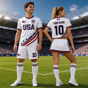 A man and a woman wearing matching white soccer uniforms with red and blue accents, standing on a soccer field.