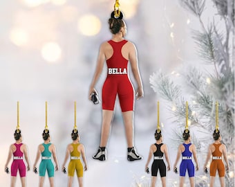 Op de afbeelding: Een verzameling worstelornamenten. De ornamenten tonen een worstelaar in verschillende kleuren, waaronder rood, roze, teal, geel, zwart, blauw en oranje. Elk ornament heeft de naam "BELLA" op de achterkant gedrukt. De ornamenten hangen aan goudkleurige touwtjes.