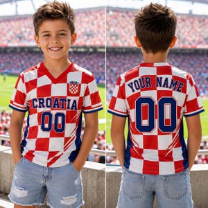 A young boy wearing a red and white Croatia soccer jersey with the number 00, standing in front of a stadium filled with spectators.