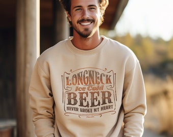 May include: Beige sweatshirt with the text "LONGNECK Ice Cold BEER Never Broke My Heart" in a vintage-style design. The sweatshirt is a neutral color and has a crew neck.
