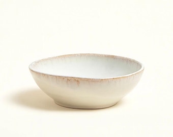 May include: A white ceramic bowl with a slightly textured surface and a light brown rim. The bowl has a simple, rounded shape and is suitable for serving food. The neutral color palette makes it versatile for various kitchen styles.