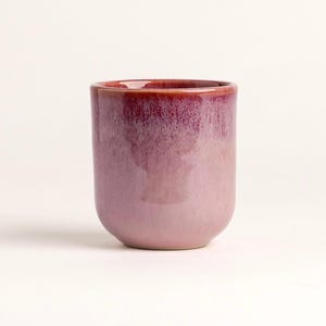 Könnte beinhalten: Ein Keramikbecher mit glänzendem Finish. Der Becher hat einen abgerundeten Boden und gerade Seiten. Die Farbe geht von einem tiefen Burgunder am Rand zu einem hellen Lavendel am Boden über. Der Innenraum ist tief burgunderfarben.