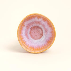 Könnte beinhalten: Eine kleine, runde Keramikschale mit lebendigem Farbschema. Die Außenseite ist ein warmes Orange, das in ein weiches rosa und weißes Innere übergeht. Das Design der Schale weist eine glatte, glänzende Oberfläche auf, ideal für kleine Portionen.