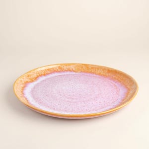 Pode incluir: Um prato de cerâmica redondo com um gradiente de cor. O centro é roxo claro, passando para uma borda pêssego e uma borda amarelo dourado. O prato tem um acabamento liso e brilhante.