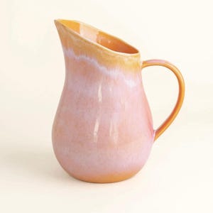 Könnte beinhalten: Eine Keramikkrug mit rundem Boden und Henkel. Der Krug ist überwiegend rosa mit einem orangefarbenen Farbverlauf am Rand und am Henkel. Der Krug hat eine glänzende Oberfläche und einen Ausguss.