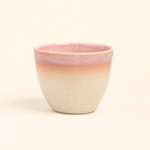 Könnte beinhalten: Eine kleine Keramiktasse mit einem gesprenkelten, cremefarbenen Boden, der in einen Pfirsich und dann in einen rosa Rand übergeht. Die Tasse hat eine glatte, matte Oberfläche und ein schlichtes, minimalistisches Design.