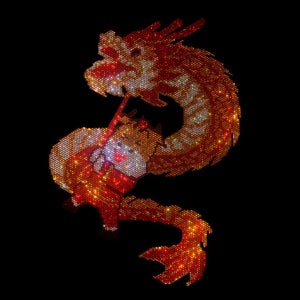May include: A red and gold dragon made of rhinestones. The dragon is curled up in a circle, with its head facing the right. The dragon's eyes are black and its scales are shiny.