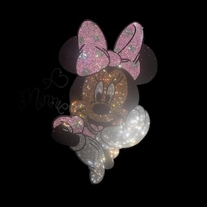 May include: A glittering Minnie Mouse design, with a pink bow and dress, and a heart with the word "Minnie". The design is made of many small, sparkling rhinestones, creating a dazzling effect against a black background.