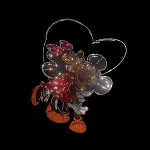 May include: A sparkling rhinestone design featuring Mickey and Minnie Mouse embracing within a heart-shaped outline. Minnie wears a red dress and bow, while Mickey is in gold and silver rhinestones. The design is set against a black background.