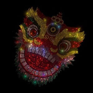 May include: A red, yellow, and green lion dance mask made of rhinestones. The mask has a large, open mouth with sharp teeth and a pair of large, round eyes.