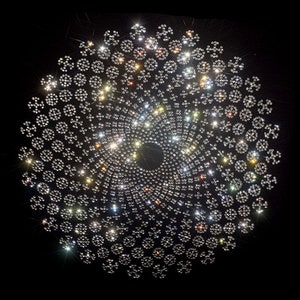 Op de afbeelding: Een cirkelvormig ontwerp gemaakt van kleine, glinsterende strassstenen die in een spiraalvorm op een zwarte achtergrond zijn gerangschikt.