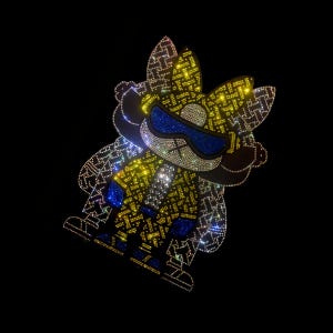 May include: A rhinestone-studded cartoon character in yellow, blue, and silver. The character has sunglasses and a patterned design. The background is black.