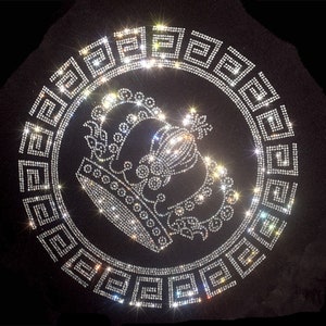 Könnte beinhalten: Ein schwarzer Stoff-Patch mit einem silbernen Strass-Design einer Krone in einem Kreis aus griechischen Schlüsselmustern.