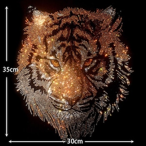 Op de afbeelding: Een close-up van een tijgergezicht gemaakt van strass. Het tijgergezicht is 30 cm breed en 35 cm hoog. De strass zijn goud, zilver en helder.