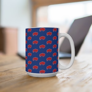 May include: White ceramic mug with a blue background and a repeating pattern of red buffalo silhouettes.