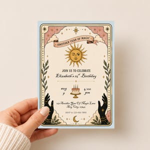 May include: A rectangular birthday invitation card featuring a central sun illustration, a cake, and two black hands reaching upward. The text reads: Another Year of Magic, Join Us to Celebrate Elizabeth's 25th Birthday, Aug 9, 4:00 pm, 123 Another Year of Magic Lane, Any City, 12345, RSVP to 123-456-7890.