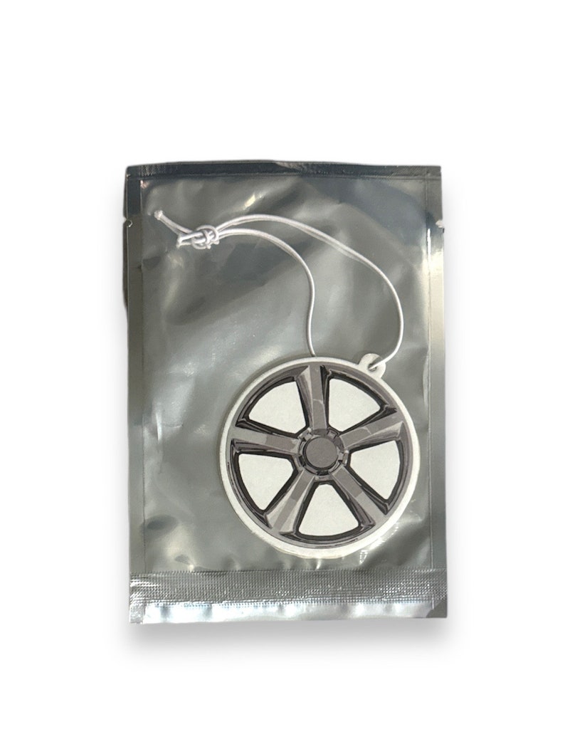 May include: A white car air freshener shaped like a wheel with a black rim and five spokes. The air freshener is packaged in a silver plastic bag with a white string.